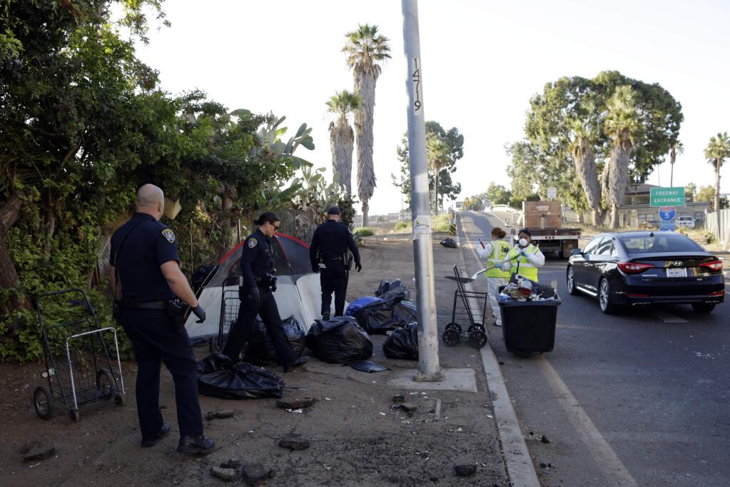 FILE - In this Sept. 25, 2017, file photo, police officers remove a tent left by the homeless in San Diego during ongoing efforts to sanitize neighborhoods to control the spread of hepatitis A. A San Diego County grand jury report faults local response to a recent hepatitis A epidemic and recommends improving lines of communication to prepare for future health emergencies. The San Diego Union-Tribune newspaper says the 20-page report released Thursday, May 17, 2018, commends officials for effectively contacting at-risk residents and getting them vaccinations. (AP Photo/Gregory Bull, File)
