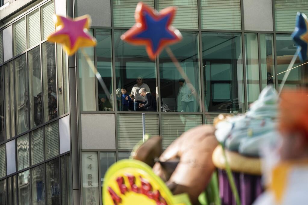 People watch the balloons moving along Sixth Avenue from an office during the Macy's Thanksgiving Day Parade in New York, Thursday, Nov. 28, 2019, in New York. (AP Photo/Jeenah Moon)