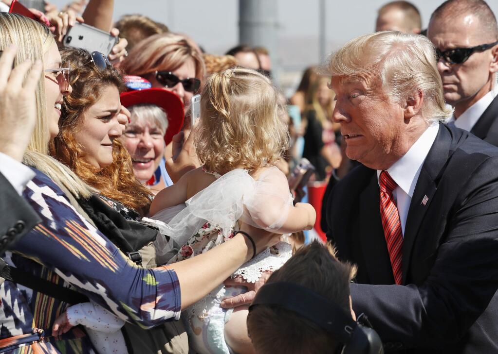 President Donald Trump struggles to hold a baby as he greets supporters as he arrives in Reno, Nev., Wednesday, Aug. 23, 2017. (AP Photo/Alex Brandon)