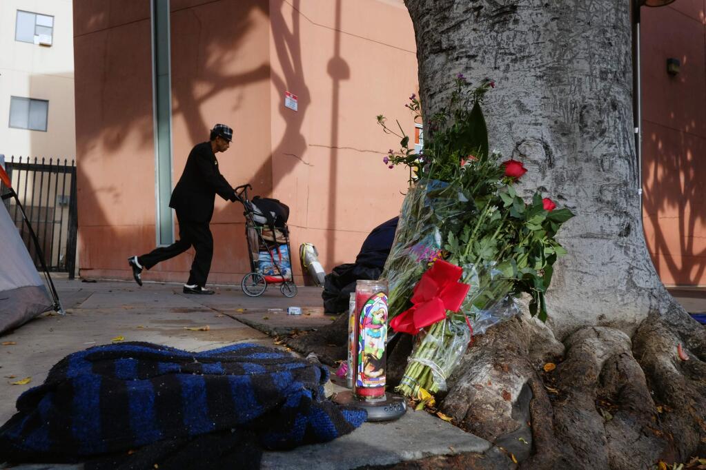 A pedestrian walks past flowers and candles placed on a sidewalk near where a man was shot and killed by police in the Skid Row section of downtown Los Angeles, Monday, March 2, 2015. Three Los Angeles police officers shot and killed the man on Sunday, as they wrestled with him on the ground, a confrontation captured on video that millions have viewed online. Authorities say the man was shot after grabbing for an officer's gun. (AP Photo/Richard Vogel)