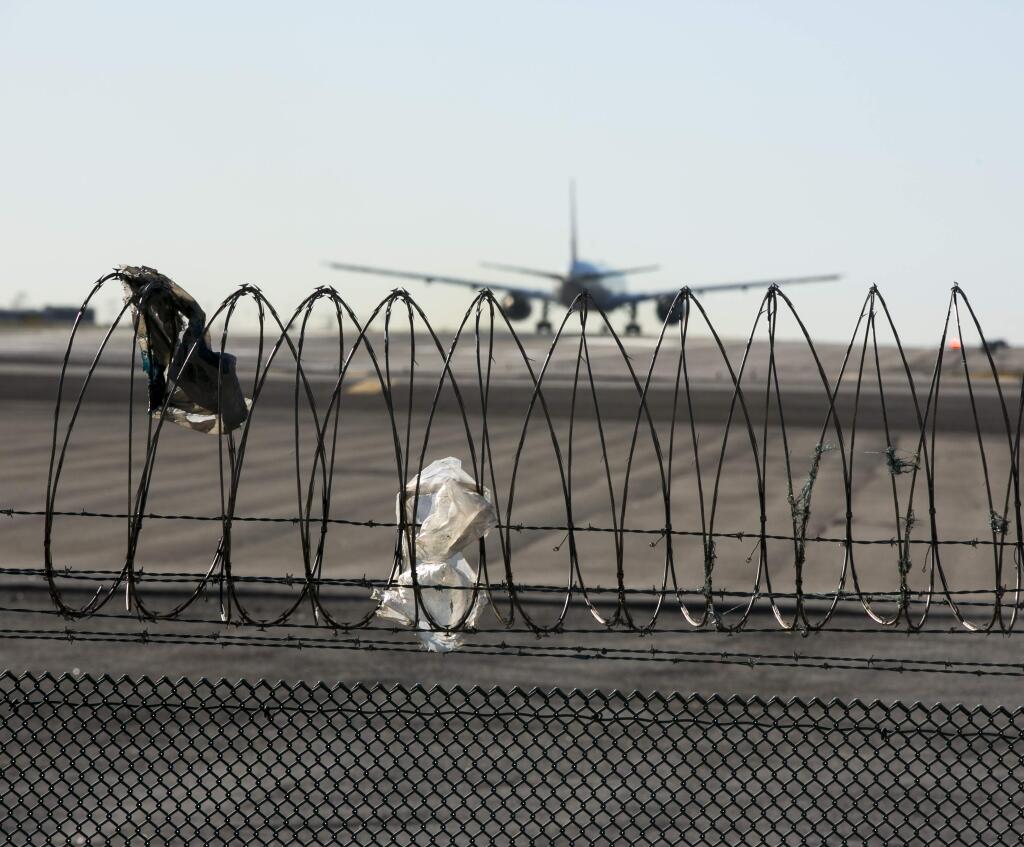 In this Friday, Jan. 23, 2015 photo, a passenger jet touches down behind the razor wire of a perimeter fence at the Los Angeles International Airport. (AP Photo/Damian Dovarganes)