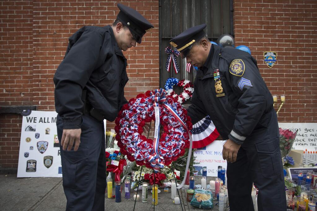 FILE - In this Monday, Dec. .22, 2014, file photo, members of the New Rochelle, N.Y. police department place a wreath at a makeshift memorial near the site where NYPD officers Rafael Ramos and Wenjian Liu were murdered in the Brooklyn borough of New York, Monday, Dec. 22, 2014. Police say Ismaaiyl Brinsley ambushed the two officers in their patrol car in broad daylight Saturday, fatally shooting them before killing himself inside a subway station. (AP Photo/John Minchillo, File)