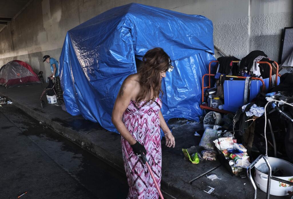 FILE - In this Oct. 19, 2018, file photo, a homeless woman, who only went by the name Angel, sweeps up the street by her tent under a freeway overpass in downtown Los Angeles. A federal judge has ordered Los Angeles city and county to move thousands of homeless people who are living near freeways, saying their health is at risk from pollution and the coronavirus. (AP Photo/Richard Vogel, File)