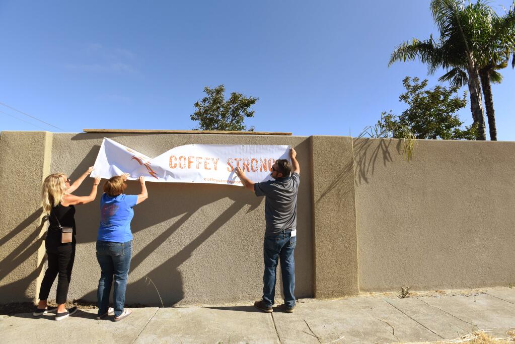 Sasha Butler, left, and Anne Barbour, center, both Coffey Park residents whose homes reside next to the Hopper Wall hang a sign with Hopper Wall project manager Steve Rahmn during the Hopper Walls Project dedication at the corner of Coffey Lane and Hopper Avenue on Saturday morning Santa Rosa, California. 'She's like our neighborhood mom,' said Butler about her neighbor Anne Barbour which both are also on the Coffey Strong board. August 24, 2019.(Photo: Erik Castro/for The Press Democrat)