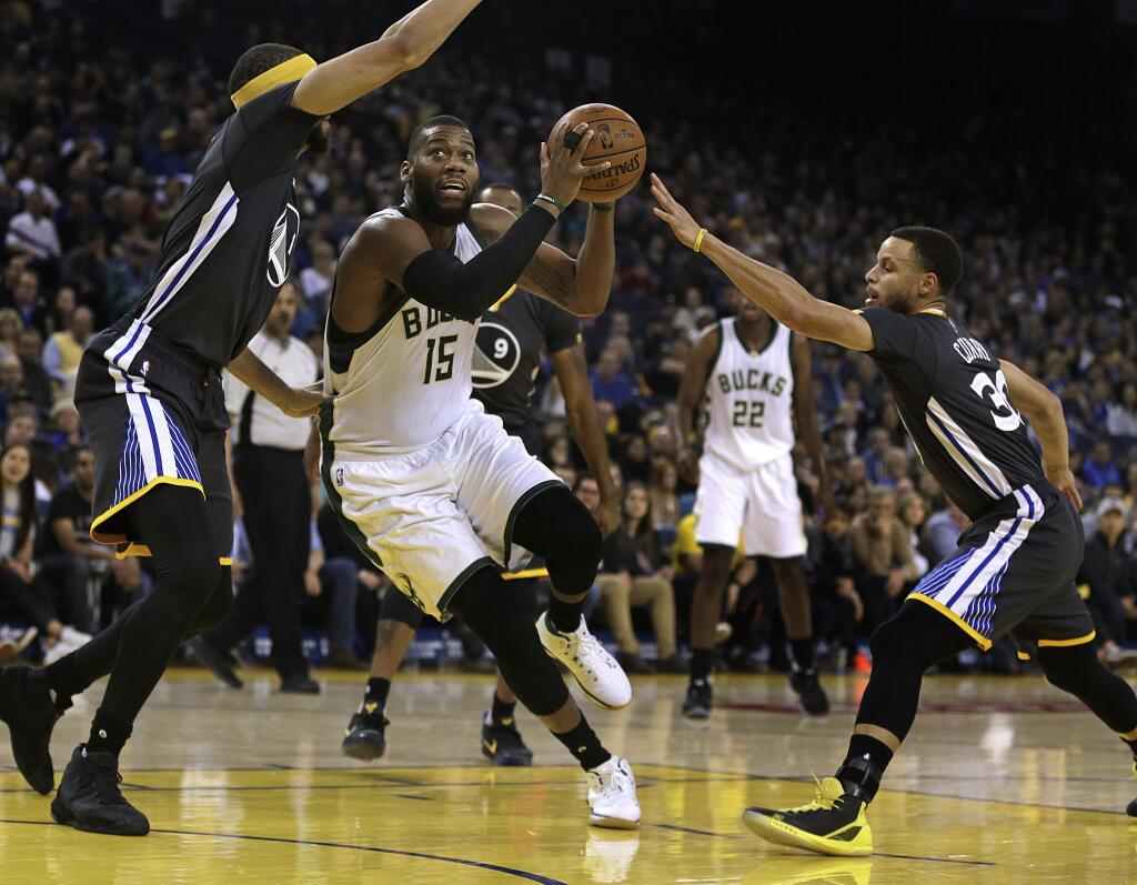 Milwaukee Bucks' Greg Monroe (15) drives the ball between Golden State Warriors' JaVale McGee, left, and Stephen Curry during the first half of an NBA basketball game Saturday, March 18, 2017, in Oakland, Calif. (AP Photo/Ben Margot)