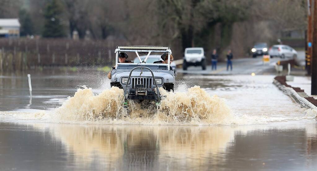 A motorist with a lifted vehicle drives through roadblocks on Highway 128 at the Alexander Valley Bridge, Monday Jan. 9, 2017. Earlier in the day, several rescues took place for those getting stranded in the water as the Russian River went over flood stage. (Kent Porter / The Press Democrat) 2017