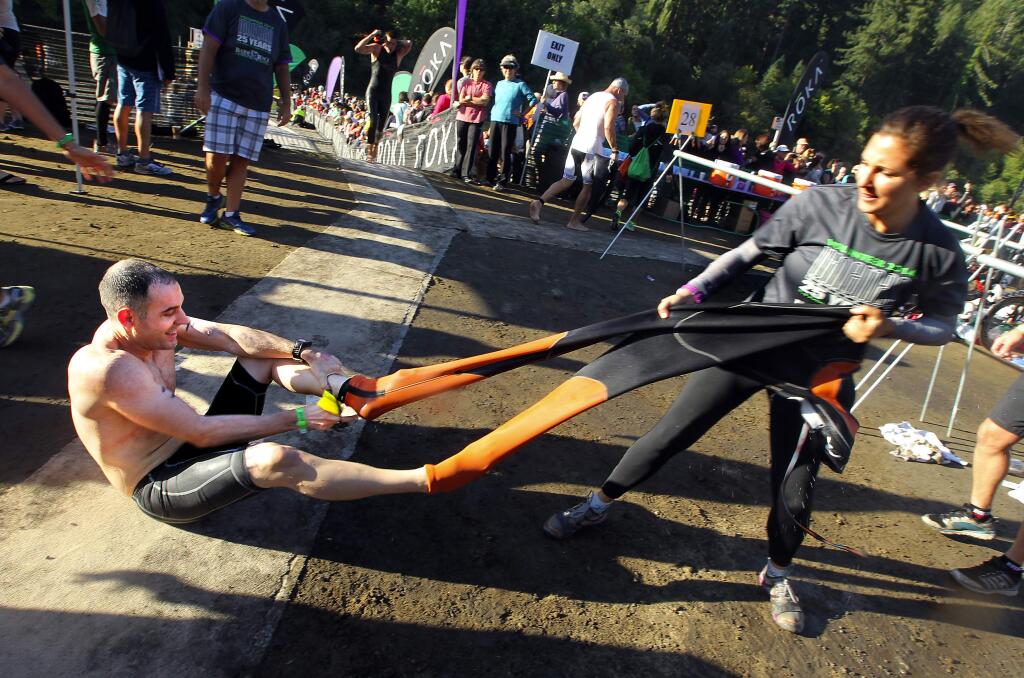 Vineman triathalon crew member Jordan Costello, right, rips the wetsuit of a competitor after the 2.4-mile swim in the Russian River at Johnson's Beach on Saturday, July 26, 2014.