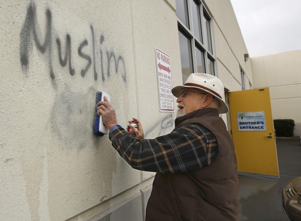 FILE - In this Feb. 1, 2017, file photo, Tom Garing cleans up racist graffiti painted on the side of a mosque in what officials called an apparent hate crime, in Roseville, Calif. A report released by the California Attorney General's office, Monday, July 9, 2018, says hate crimes jumped more than 17 percent last year, though they remain relatively rare. (AP Photo/Rich Pedroncelli, File)