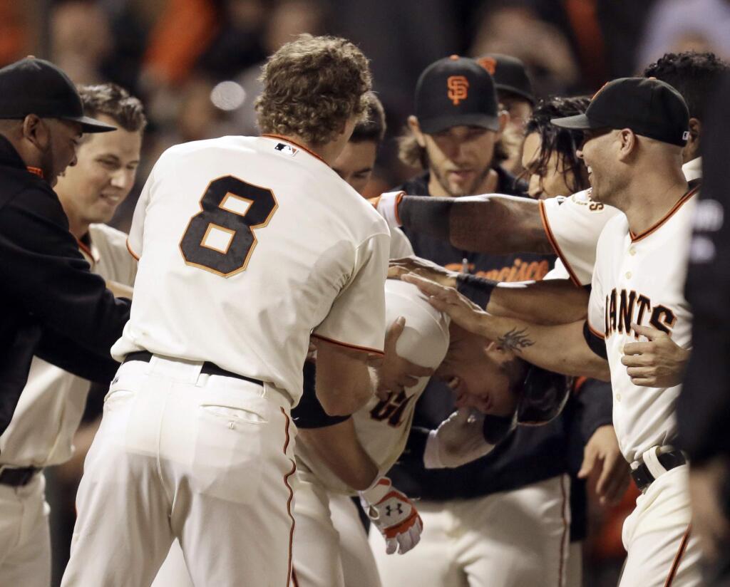 San Francisco Giants' Buster Posey, center right, bent over, is mobbed by teammates after hitting the game-winning home run off Colorado Rockies' Juan Nicasio in the ninth inning of a baseball game Wednesday, Aug. 27, 2014, in San Francisco. The Giants won 4-2. (AP Photo/Ben Margot)