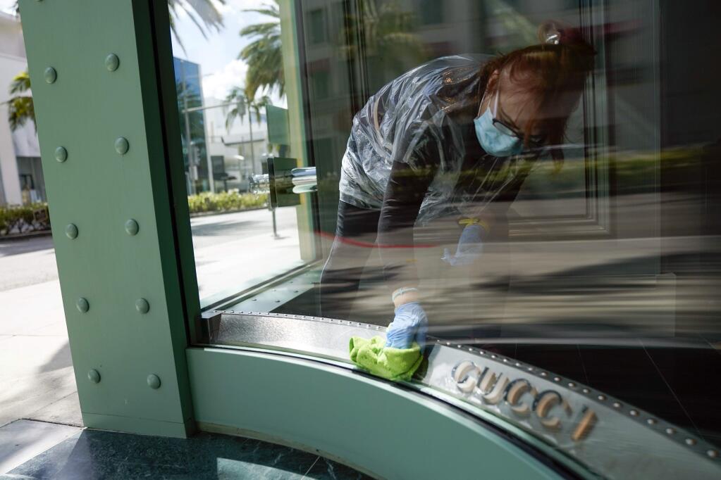 A woman wearing a face mask cleans the front windows of a Gucci store on Rodeo Drive Tuesday, May 19, 2020, in Beverly Hills, Calif. (AP Photo/Ashley Landis)