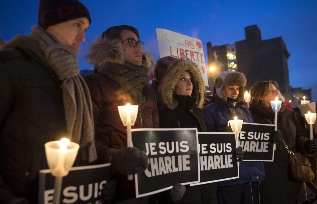 People stand in front of City Hall with a sign that reads in French 'I am Charlie' in solidarity with those killed in an attack at the Paris offices of the weekly newspaper Charlie Hebdo, during a vigil, Wednesday, Jan. 7, 2015 in Montreal. (AP Photo/The Canadian Press, Paul Chiasson)