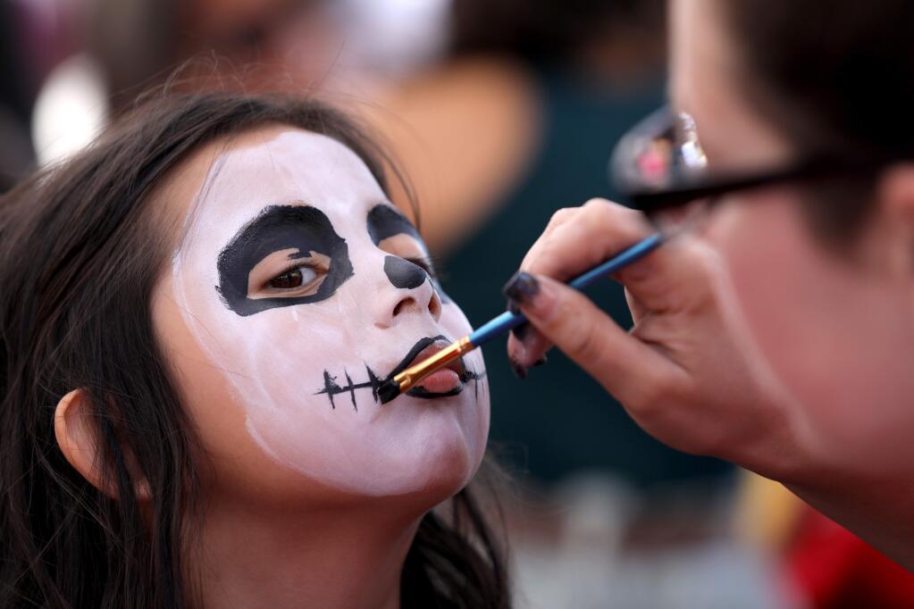 Aaliyah Chavez, 5, sits to get her face painted by volunteer Jeana Barella during a Dia de Los Muertos event at City Hall in Healdsburg on Sunday, November 24, 2019. (BETH SCHLANKER/ The Press Democrat)
