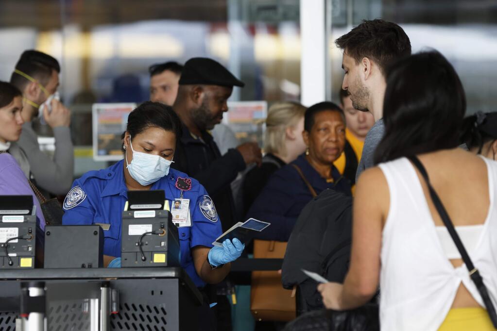 FILE - In this Saturday, March 14, 2020 file photo, a Transportation Security Administration agent hands a passport back to a traveler as she screens travelers, at a checkpoint inside an airline terminal at John F. Kennedy Airport in New York. The coronavirus pandemic that's caused many Americans to avoid airports has others booking spur-of-the moment trips at dirt-cheap ticket prices. (AP Photo/Kathy Willens, File)