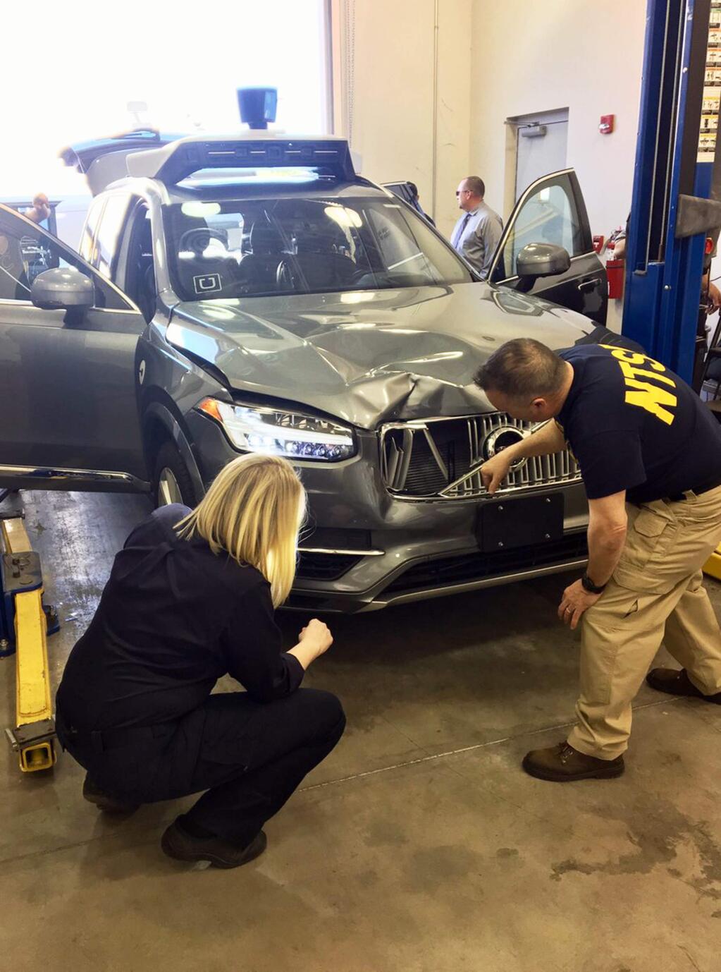 FILE - In this March 20, 2018 file photo provided by the National Transportation Safety Board, investigators examine a driverless Uber SUV that fatally struck a woman in Tempe, Ariz. An Arizona police report says the human backup driver the Uber autonomous SUV was streaming a television show on Hulu just before the vehicle struck and killed a pedestrian in March. The Arizona Republic reported that the driver was watching “The Voice,” a television musical talent show. The newspaper received the more than 300-page report from Tempe police on Thursday, June 21. (National Transportation Safety Board via AP)