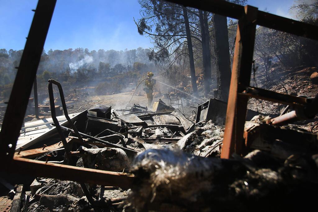 A Cal Fire firefighter who declined to give his name, douses hot spots around a trailer that was destroyed during the Grade fire off Jerusalem Valley Road in Lake County, Monday Aug. 24, 2015. (KENT PORTER/ PD FILE)