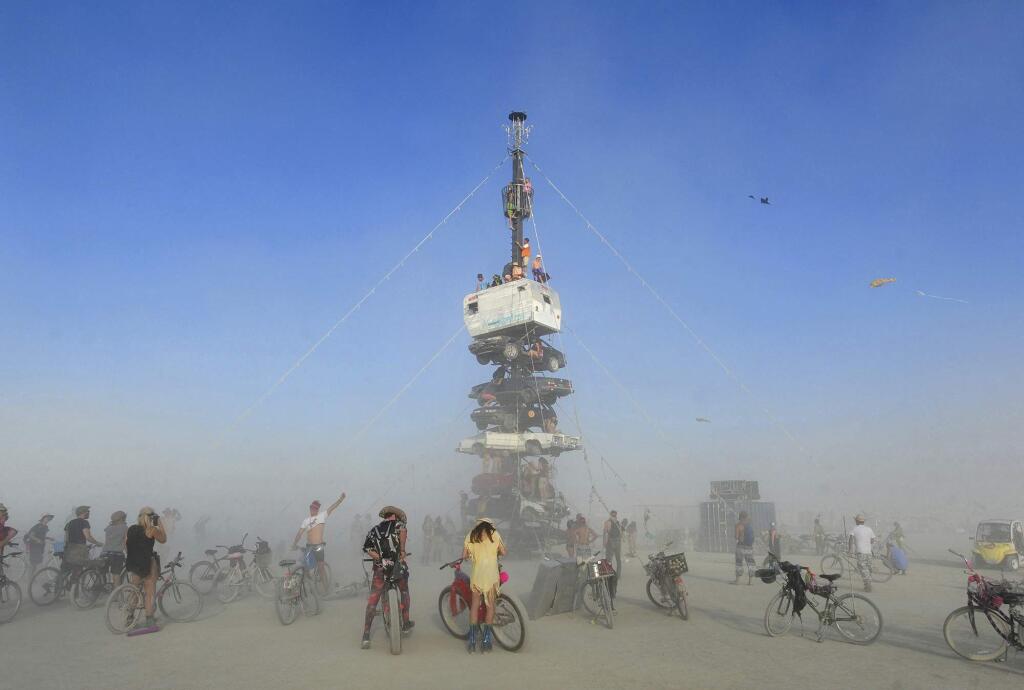 FILE - this Monday, Aug. 27, 2018 file photo, burners surrounded by playa dust climb onto an art installation titled, 'Night of the Climb,' at Burning Man, in Gerlach, Nev. (Andy Barron/The Reno Gazette-Journal via AP, File)