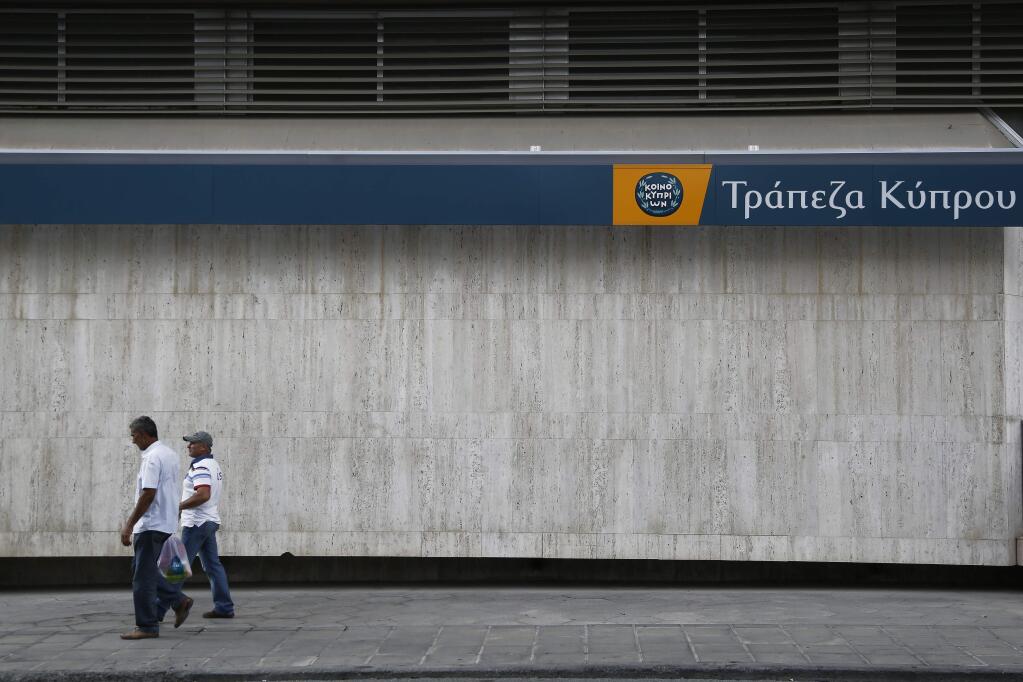 Men walk outside of a branch of Bank of Cyprus in central Nicosia, Cyprus, Sunday, Oct. 26, 2014. The European Central Bank says 13 of Europe's 130 biggest banks have flunked an in-depth review of their finances and must increase their capital buffers against losses by 10 billion euros ($12.5 billion). The Cypriot Hellenic bank is one of the 13 banks in Europe with the shortfall. (AP Photo/Petros Karadjias)