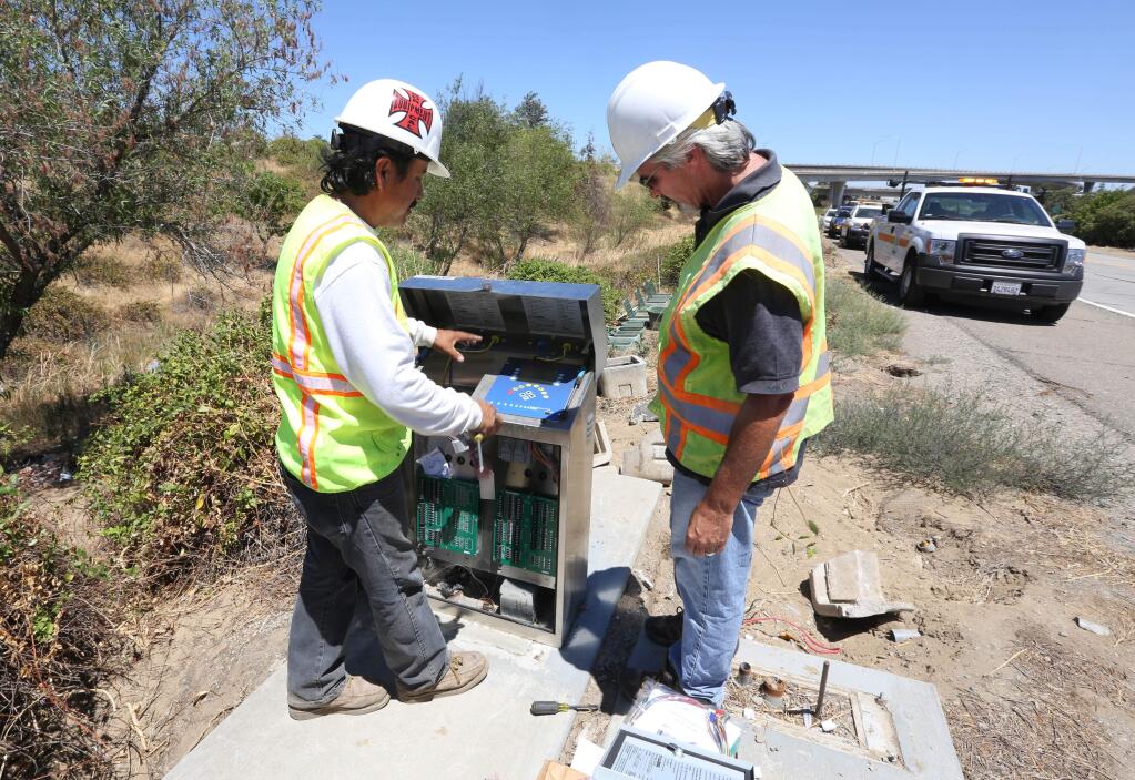 In this photo taken July 24, 2014, Russ Lake, a field inspector for the California Department of Transportation, right, looks over a remote water management controller just installed by Lionel Flores along Highway 4 in Stockton. Flores, who works for Takehara Landscaping, an irrigation contractor hired to oversee the irrigation systems along the Caltrans maintained roads in the area, was replacing a unit that had been destroyed during a car accident. From these control units, Caltrans can monitor water flow from a central office looking for excessive water usage caused by leaks or breaks in the system.(AP Photo/Rich Pedroncelli)