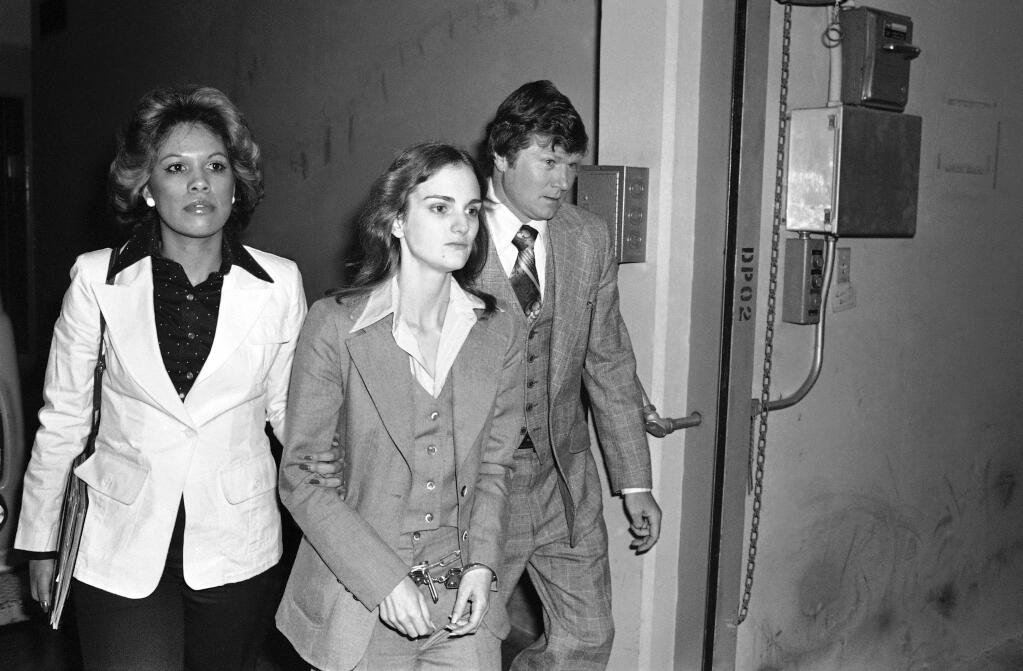 Accompanied by Deputy U.S. Marshal John Brophy, Patty Hearst, center, leaves the Federal Building in San Francisco, hours after her sentencing on a bank robbery conviction on April 12, 1976. Hearst was kidnapped and radicalized by the Symbionese Liberation Army in February 1974. (Associated Press)