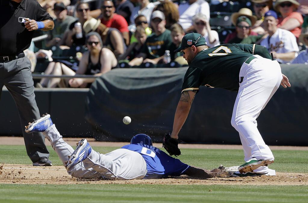 Oakland Athletics first baseman Yonder Alonso (17) cannot catch a pick off throw as Kansas City Royals' Terrance Gore slides into first base during the fourth inning of a spring training baseball game in Mesa, Ariz., Sunday, March 27, 2016. Gore advanced to second on the throwing error. (AP Photo/Jeff Chiu)