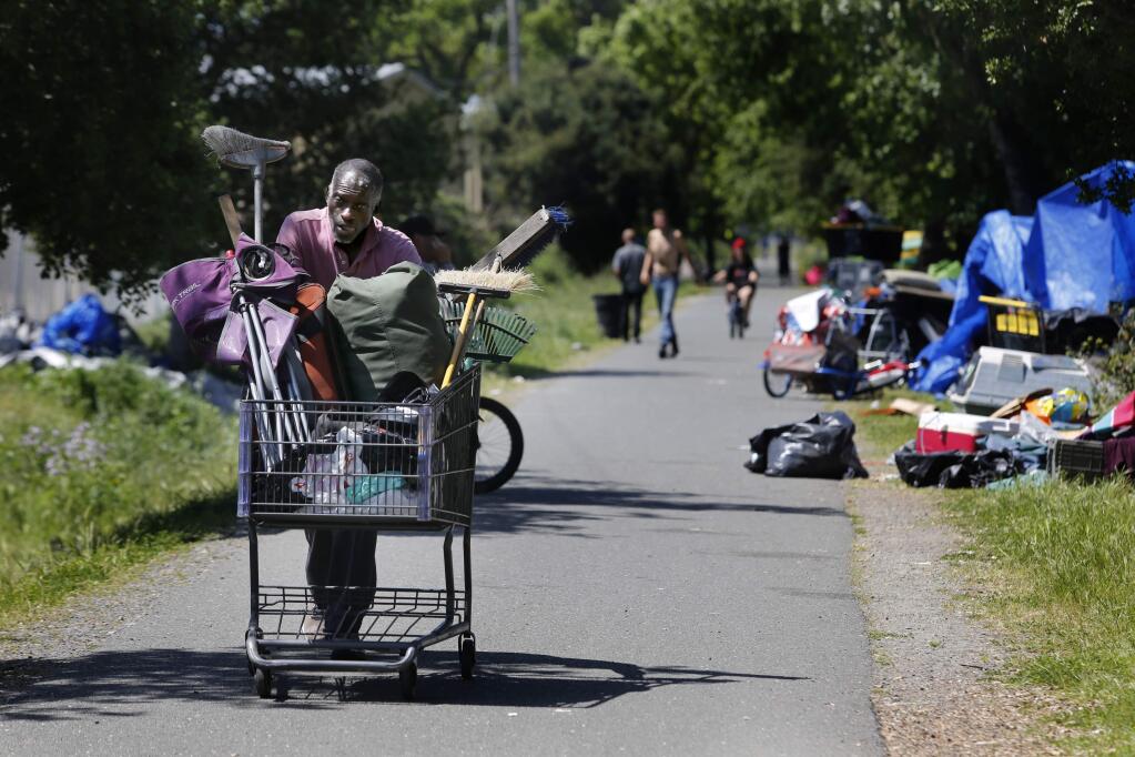 Mark M. pushes a shopping cart along the Joe Rodota Trail past homeless encampments set up next to the former Roseland homeless encampment in Santa Rosa Monday, April 23, 2018. (Beth Schlanker/ The Press Democrat)