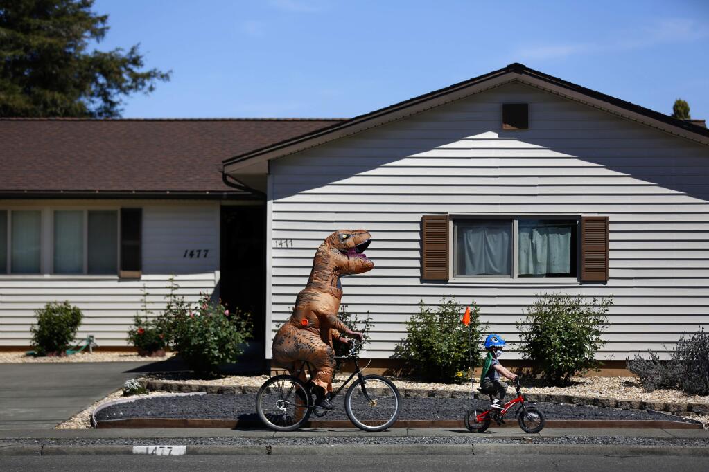 Dan Sartin, dressed in an inflatable dinosaur costume and his son, Leo, 4, ride their bikes along Russell Ave in Santa Rosa, California on Tuesday, April 14, 2020. (BETH SCHLANKER/ The Press Democrat)