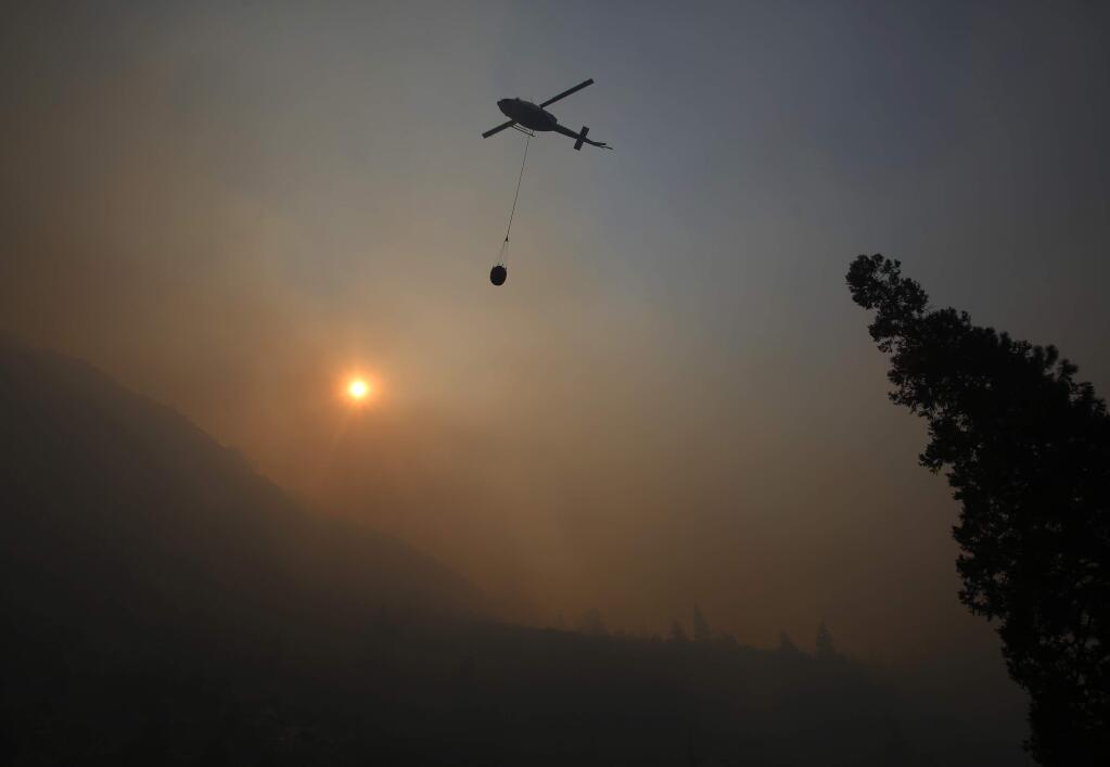 A fire helicopter takes off through smoke rising to make a drop on active fires in Yosemite National Park after the park reopened after a three week closure from smoke and fires that led to most tourists canceling their trips Tuesday, Aug. 14, 2018 in Yosemite, Calif. (AP Photo/Gary Kazanjian)