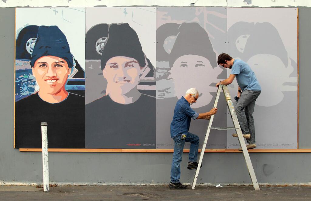 A mural of Andy Lopez that was mounted last fall to the side of a vacant Roseland gas station can now be found on the side of the Peace and Justice Center. Artist Mario Uribe (left) and his assistant, Daniel Doughty (right) are shown here as they hang it in its original location. (John Burgess / Press Democrat)