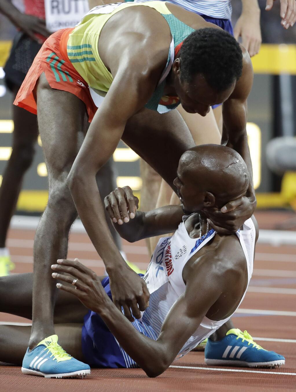 Ethiopia's Muktar Edris helps Britain's Mo Farah to his feet after winning gold in the Men's 5000m during the World Athletics Championships in London Saturday, Aug. 12, 2017. (AP Photo/David J. Phillip)