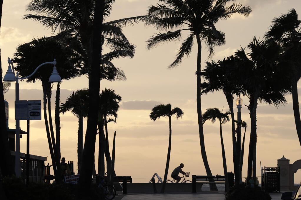 A cyclist rides along the Hollywood Beach Boardwalk at sunrise during the new coronavirus pandemic, Wednesday, May 13, 2020, in Hollywood, Fla. The Boardwalk opened Tuesday for the first time since the pandemic started, and is open for limited hours daily for exercise only. Broward County beaches remain closed. (AP Photo/Lynne Sladky)