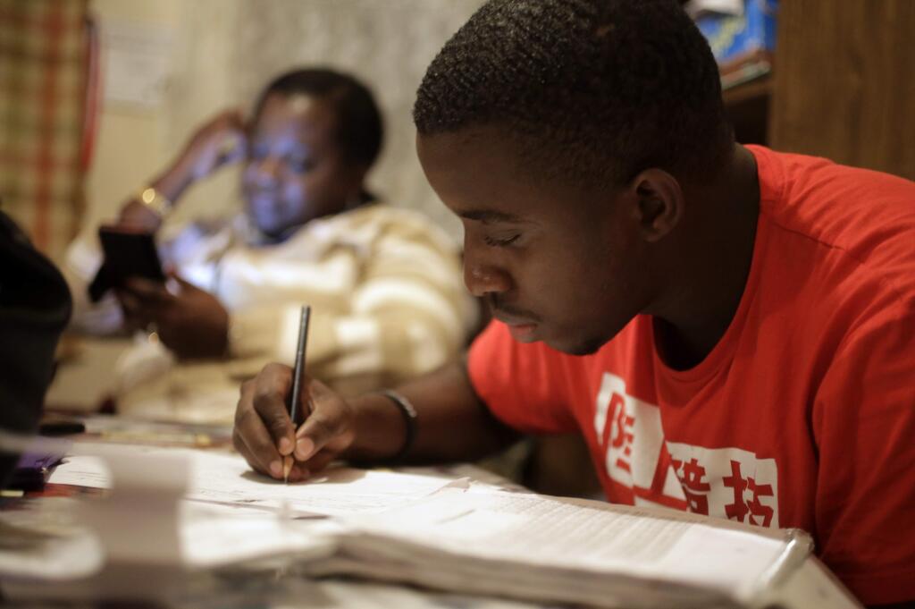 In this Wednesday, Nov. 15, 2017 photo, Amocachy Jeune, right, does homework as his mother Marianne Jeune, left, a Haitian immigrant staying in the U.S. through the Temporary Protected Status program, sits nearby at their Boston home. She has worked a variety of jobs caring for the elderly, after she lost her home in Haiti in the 2010 earthquake. The U.S. administration said Tuesday, Nov. 21, 2017, it is ending a temporary residency permit program that has allowed almost 60,000 citizens from Haiti to live and work in the United States since a powerful earthquake shook the Caribbean nation in 2010. The Homeland Security Department said the benefit will be extended one last time - until July 2019 - to give Haitians time to prepare to return home. (AP Photo/Steven Senne)