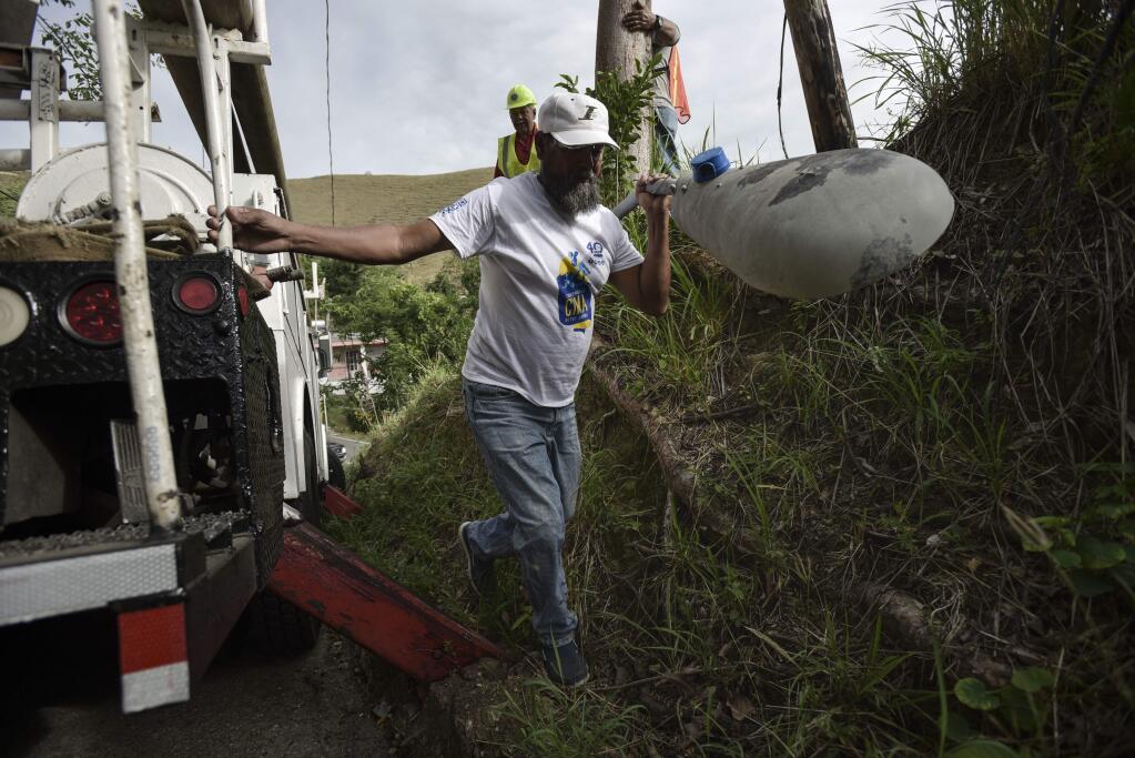 In this Jan. 31, 2018 photo, El Progreso resident Felix Rodriguez Colon removes a broken road light as he helps municipal workers restore power lines, four months after Hurricane Maria hit the town of Coamo, Puerto Rico. Brigades of city volunteers helping to restore power include teachers, handymen, a postal worker and an accountant, backed by municipal workers with professional equipment, tools and experience in light electrical work. (AP Photo/Carlos Giusti)