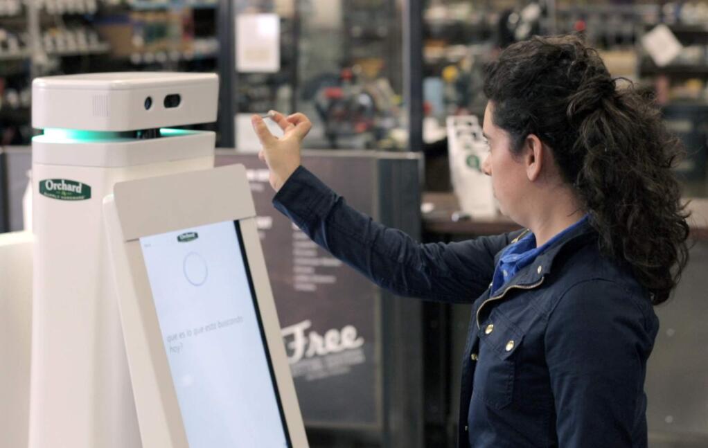 In this undated image provided by Lowe's, a woman holds a nail up to be scanned by an OSHbot robot. The robots are equipped with 3D cameras so they can scan and identify items. And customers can research items they want to buy on their screen. Then the robot can lead them to the aisle where an item is located. (AP Photo/Lowe's)