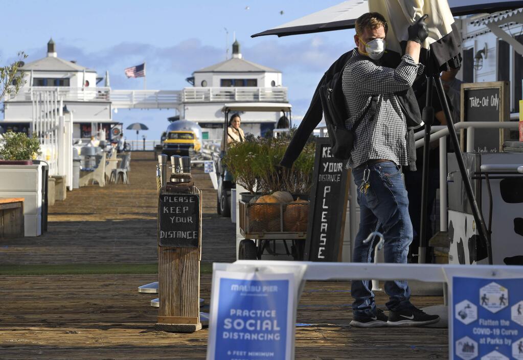 Signs are seen advising people to keep their distance from each other as a worker removes an umbrella in front of a restaurant on the Malibu Pier, Monday, March 23, 2020, in Malibu, Calif. Officials are trying to dissuade people from using the beaches after California Gov. Gavin Newsom ordered the state's 40 million residents to stay at home indefinitely. His order restricts non-essential movements to control the spread of the coronavirus that threatens to overwhelm the state's medical system. (AP Photo/Mark J. Terrill)
