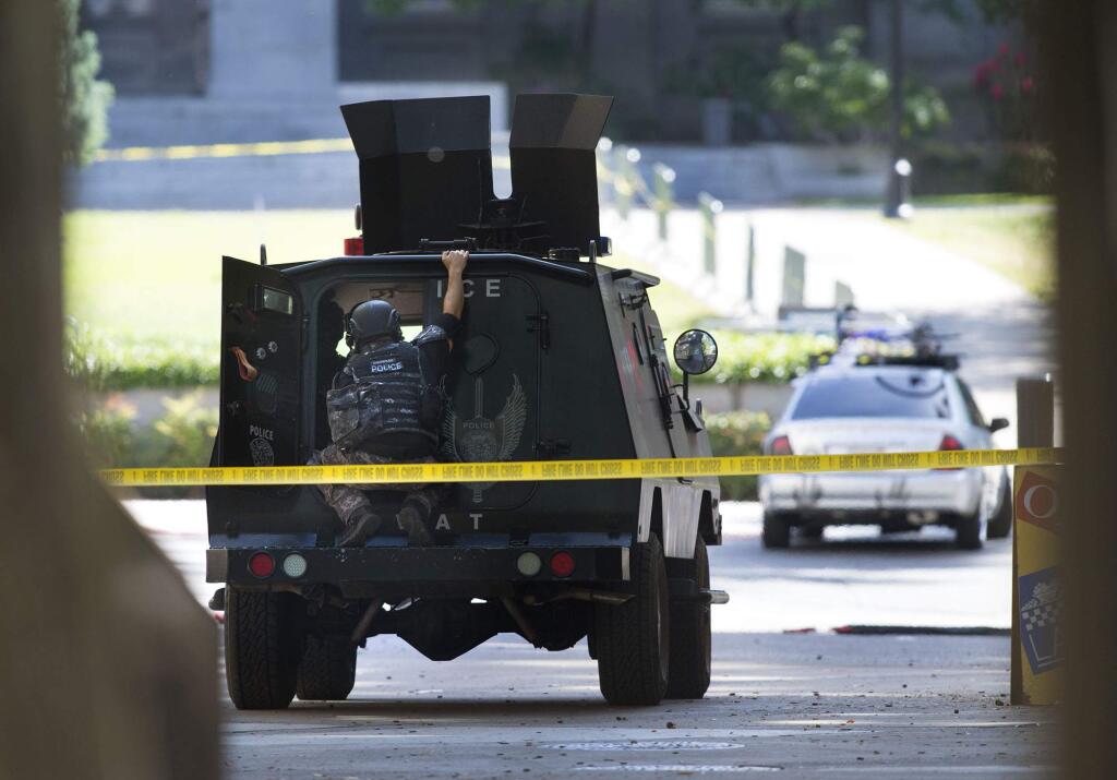 A SWAT team member watches as a man barricades himself in his car while blocking an intersection on the north side of the state Capitol Monday, April 18, 2016 in Sacramento, Calif. A standoff near the California Capitol is over after a vehicle covered in scribbled writing blocked traffic and stalled business for several hours. Sacramento police said a suspect in a suspicious car voluntarily surrendered Monday. (Randy Pench/The Sacramento Bee via AP)