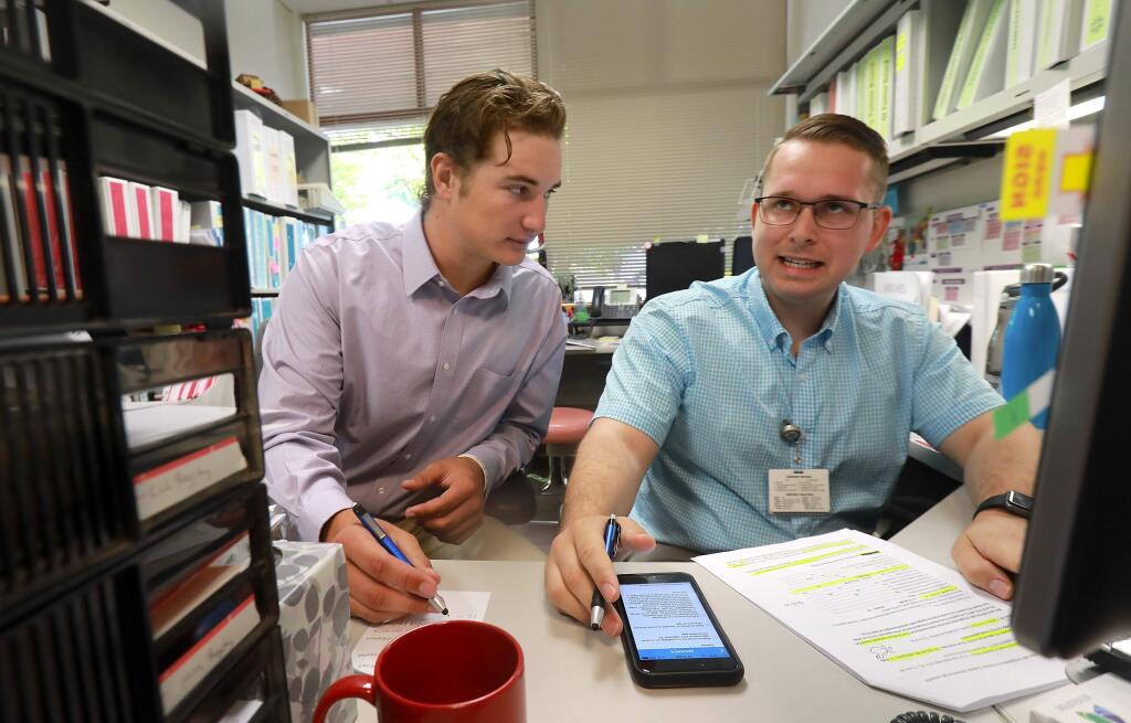 Intern Alec Rennard, left, works with Clinical Research Coordinator Anthony Blackburn to identify possible candidates for breast cancer clinical trials in the St. Joseph Health cancer care center in Santa Rosa. Renaud is pitching this summer for the Healdsburg Prune Packers before returning to Michigan University in the fall. (John Burgess / The Press Democrat)