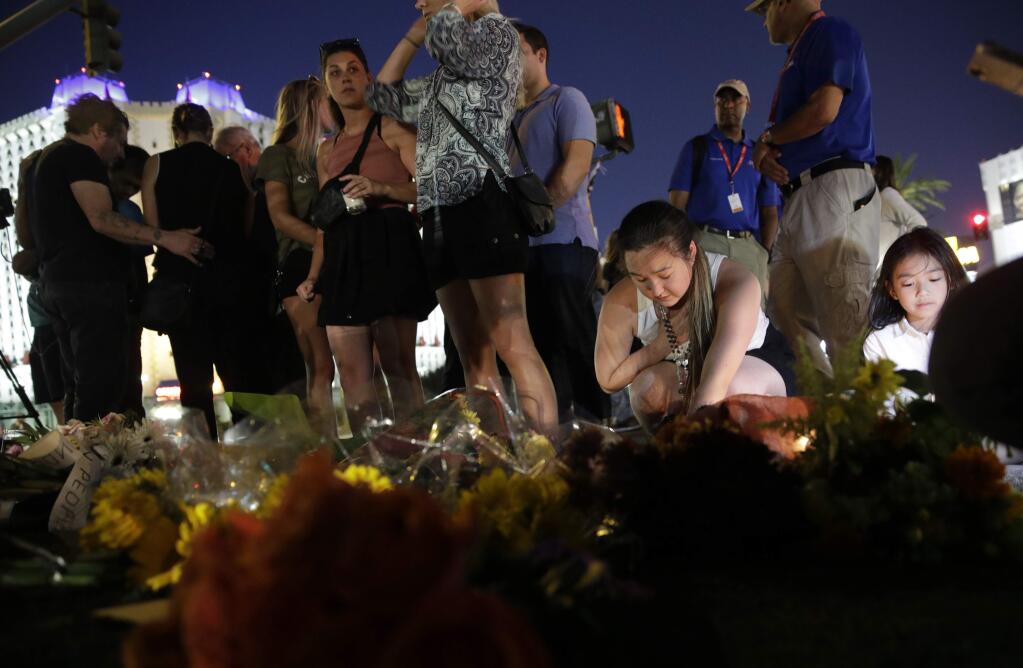 People pause at a memorial set up for victims of a mass shooting in Las Vegas, on Tuesday, Oct. 3, 2017. A gunman opened fire on an outdoor music concert on Sunday. It was the deadliest mass shooting in modern U.S. history, with dozens of people killed and hundreds injured, some by gunfire, some during the chaotic escape. (AP Photo/John Locher)