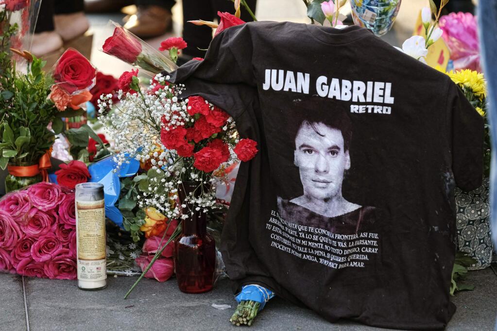 A T-shirt is left along with flowers and candles at the Hollywood star of Mexican superstar Juan Gabriel, in the Hollywood section of Los Angeles on Monday, Aug. 29, 2016. Gabriel a songwriter and singer who was an icon in the Latin music world, died Sunday at his home in California at age 66. (AP Photo/Richard Vogel)