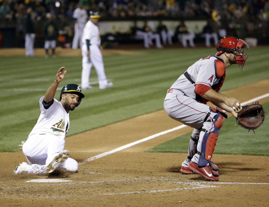 Oakland Athletics' Marcus Semien, left, scores past Los Angeles Angels catcher Chris Iannetta after a double by Ike Davis during the sixth inning of a baseball game Wednesday, April 29, 2015, in Oakland, Calif. (AP Photo/Marcio Jose Sanchez)