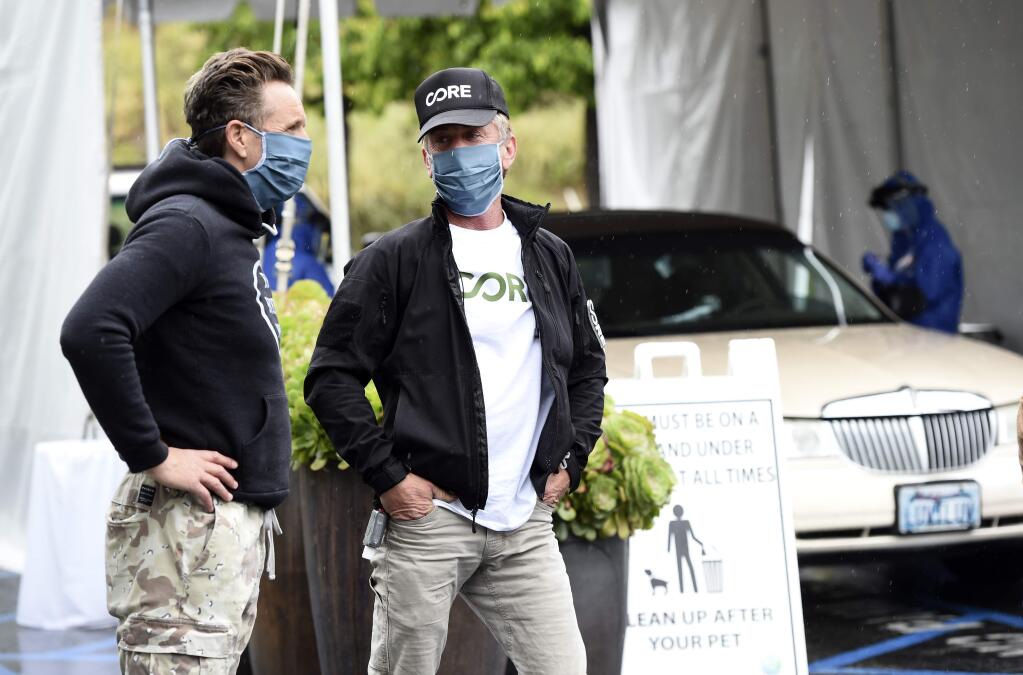 In this April 9, 2020 photo, actor Sean Penn, center, founder of the nonprofit organization Community Organized Relief Effort, talks with CORE supporter and MGM Worldwide Television Group chairman Mark Burnett at a CORE-sponsored coronavirus testing site at Malibu City Hall in Malibu, Calif. The Oscar winner's disaster relief organization called CORE has teamed up with Los Angeles Mayor Eric Garcetti's office and the city's fire department to safely distribute free drive-through COVID-19 test sites for those with qualifying symptoms. (AP Photo/Chris Pizzello)