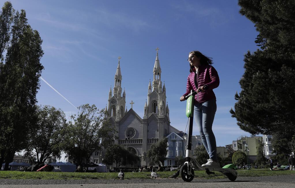 A woman rides a motorized scooter in Washington Square Park in San Francisco. Gov. Jerry Brown signed legislation Wednesday, Sept. 19, 2018, requiring helmets only for people under age 18 while riding motorized scooters. It's a win for companies such as Bird and Lime that operate the popular scooters in major cities across California and the country. (AP Photo/Jeff Chiu, File)