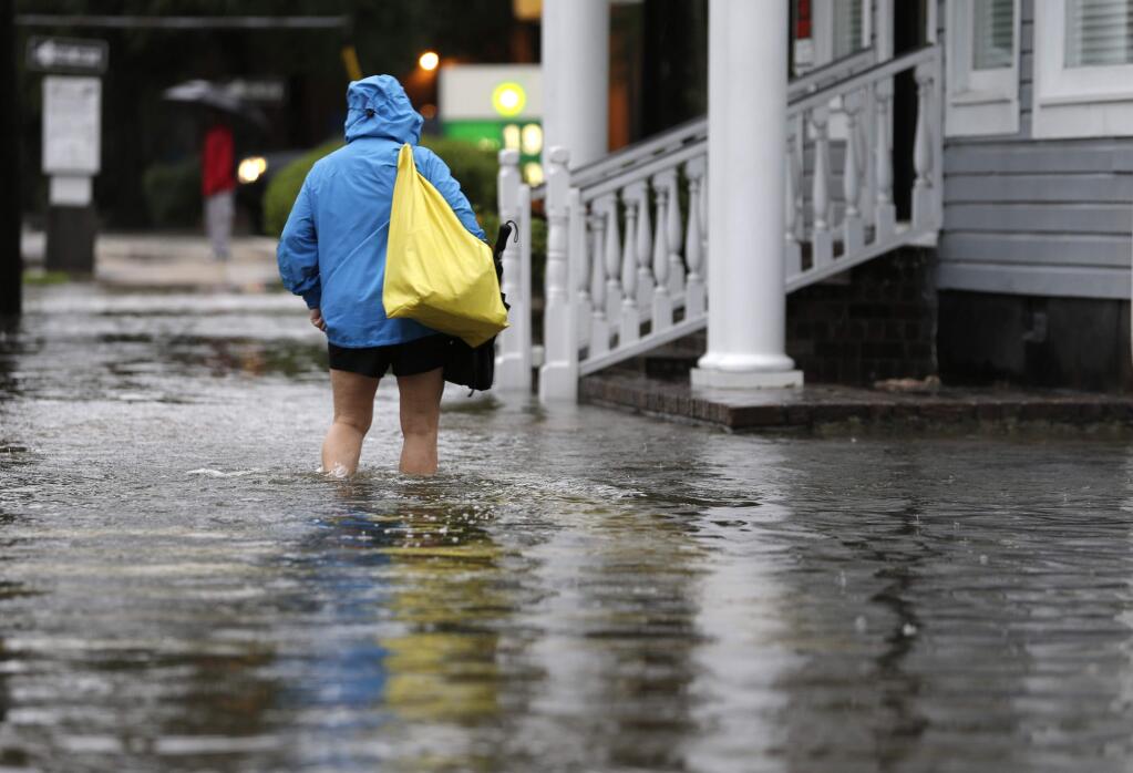 A woman walks down a flooded sidewalk toward an open convenience store in Charleston, S.C., Sunday, Oct. 4, 2015. President Barack Obama declared a state of emergency in South Carolina and ordered federal aid to bolster state and local efforts as flood warnings remained in effect for many parts of the East Coast through Sunday. (AP Photo/Chuck Burton)