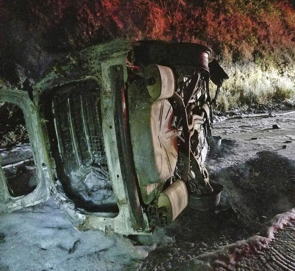 This Aug. 3, 2019 photo from the Hoopa Fire Department shows a Humboldt County Sheriff's Department patrol car after it was struck by a falling bear and then hit an embankment, rolled onto its side and burst into flames, near Hoopa, Calif., in Northern California. The deputy managed to escape without serious injury. (Rod Mendes/Hoopa Fire Department via AP)