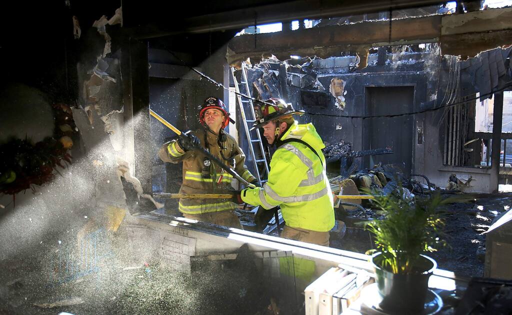 Firefighters punch a wall looking for hot spots at the Russian River Health Center on Third Street, the interior and exterior of the building suffered major damage in the overnight fire, Saturday Dec. 26, 2015. (Kent Porter / Press Democrat) 2015