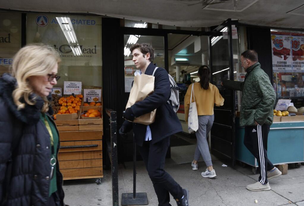 In this March 17, 2020, photo, Liam Elkind, 20, leaves the Associated Supermarket with a bag of groceries including salad ingredients and fresh produce for 83-year-old Carol Sterling, who is self-quarantined in her apartment in New York due to the coronavirus outbreak. Elkind, a junior at Yale, and his friend, Simone Policano, amassed about 1,300 volunteers in 72 hours to deliver groceries and medicine to older New Yorkers and others most vulnerable since the virus swept the city. They call themselves Invisible Hands, and they do something else in the process, provide some human contact and comfort, at a safe distance, of course. (AP Photo/Jessie Wardarski)