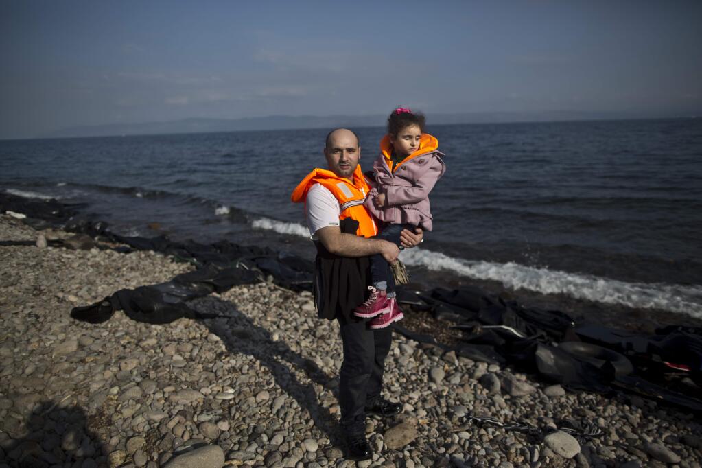 In this photo taken on Saturday, Oct. 3, 2015, Syrian refugee Mahmoud Naoura, 30, who came from Aleppo, Syria, poses for a picture while holding his daughter Huda, 5, who was injured in 2012 by a government bombing on their home which made her lose her sight, shortly after arriving on a dinghy from the Turkish coast to the northeastern Greek island of Lesbos. Naoura said 'I just want to cure my daughter. Huda will see again, inshallah, and when she will open her eyes I want her to see a safe environment around.' (AP Photo/Muhammed Muheisen)