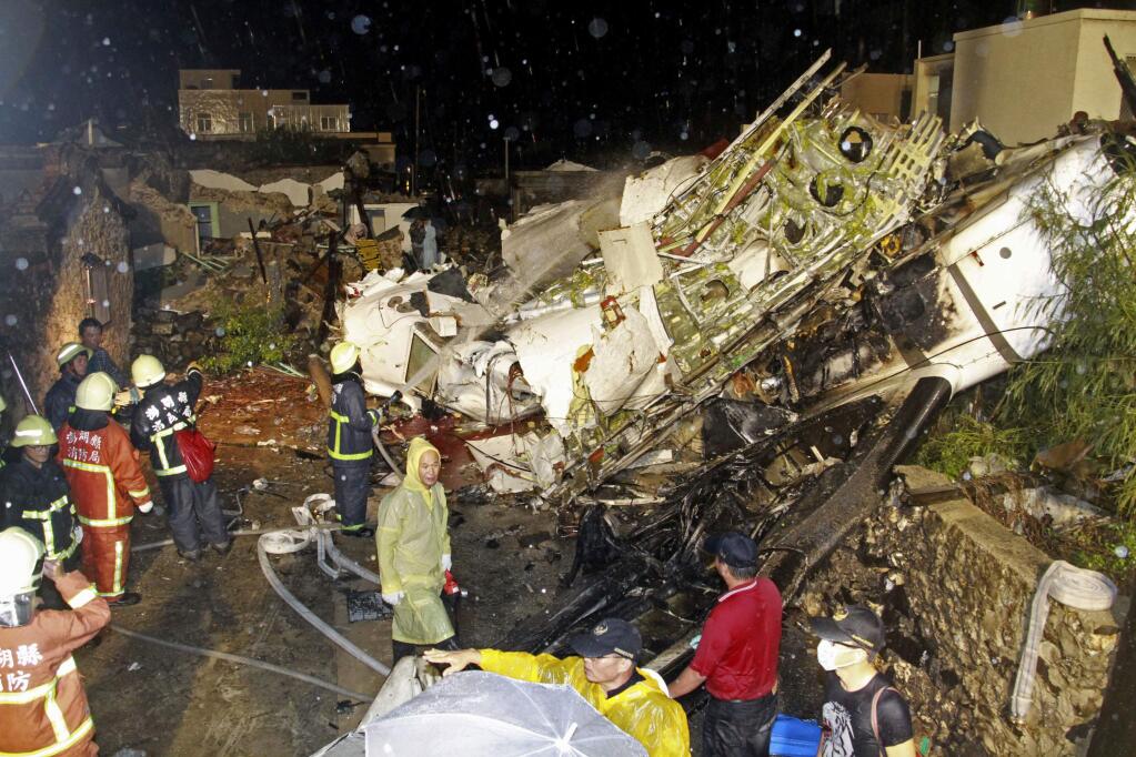 Rescue workers work next to the wreckage of TransAsia Airways flight GE222 which crashed while attempting to land in stormy weather on the Taiwanese island of Penghu, late Wednesday, July 23, 2014. A plane landing in stormy weather crashed outside an airport on a small Taiwanese island late Wednesday, and a transport minister said dozens of people were trapped and feared dead. (AP Photo/Wong Yao-wen)