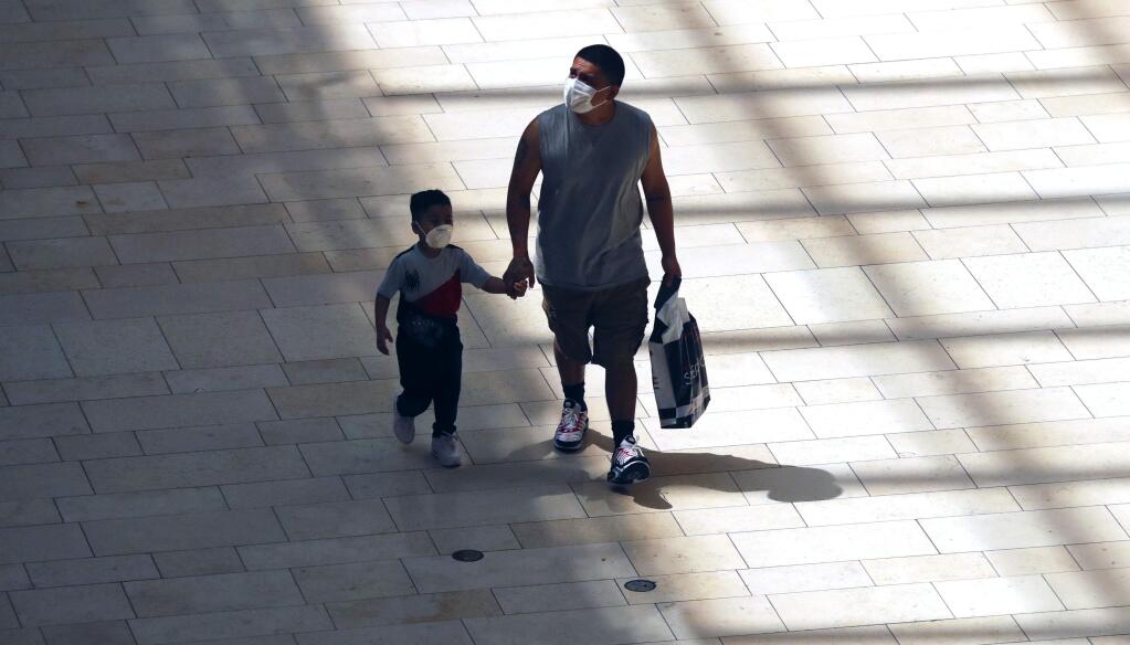 Amid concerns of the spread of COVID-19, a man and little boy walk hand-in-hand while wearing masks in shadows cast by sunlight at the Galleria Dallas mall in Dallas, Monday, May 4, 2020. (AP Photo/LM Otero)