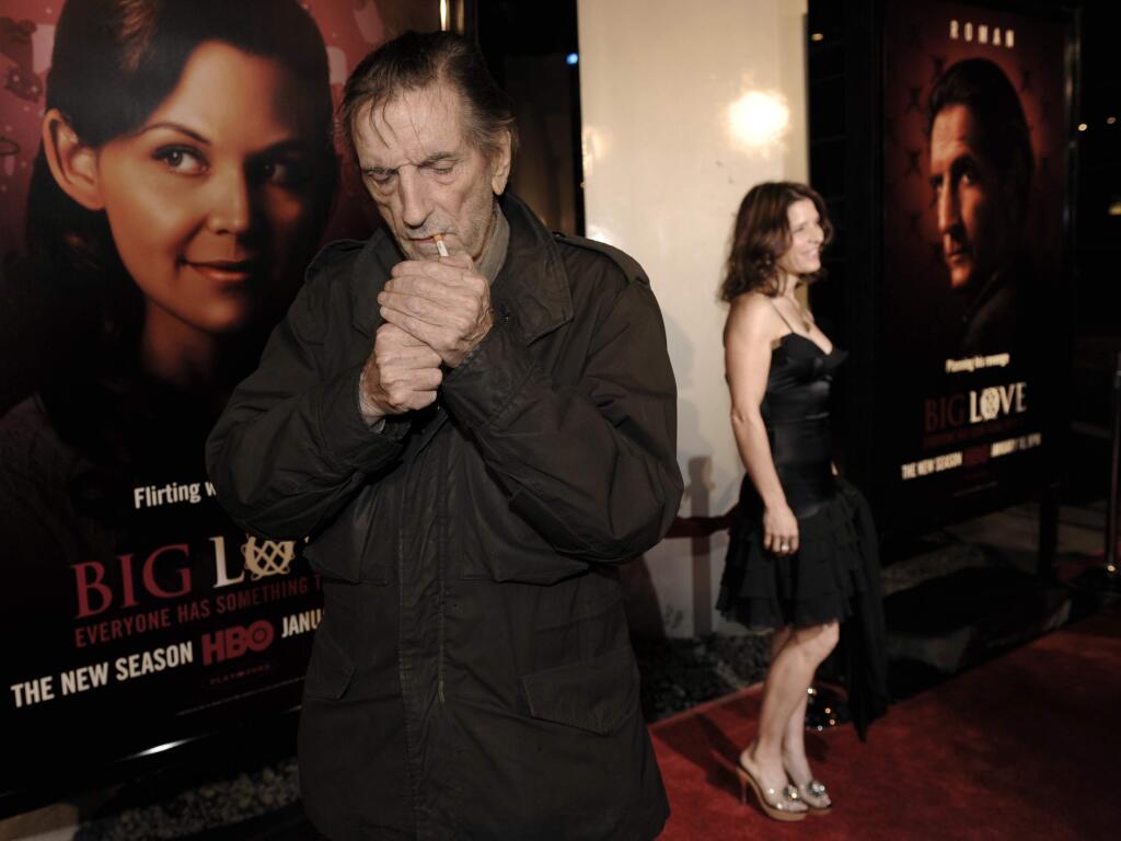FILE - In this Jan. 14, 2009, file photo, actor Harry Dean Stanton, left, a cast member in the HBO series 'Big Love,' lights a cigarette as fellow cast member Melora Walters poses on the red carpet at the show's third season premiere in Los Angeles. Legendary character actor Stanton has died at age 91. Stanton's agent John S. Kelly says the actor died of natural causes Friday afternoon, Sept. 15, 2017, at Cedars-Sinai Medical Center in Los Angeles. (AP Photo/Chris Pizzello, File)