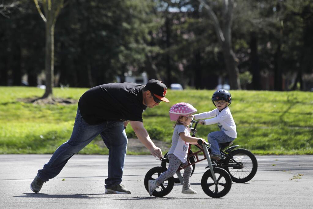 Jamison Linebaugh helps his children Charlotte, 2, and Jackson, 4, learn to ride their bikes at Sunrise Park on Monday, March 26, 2018 in Rohnert Park, California . (BETH SCHLANKER/The Press Democrat)